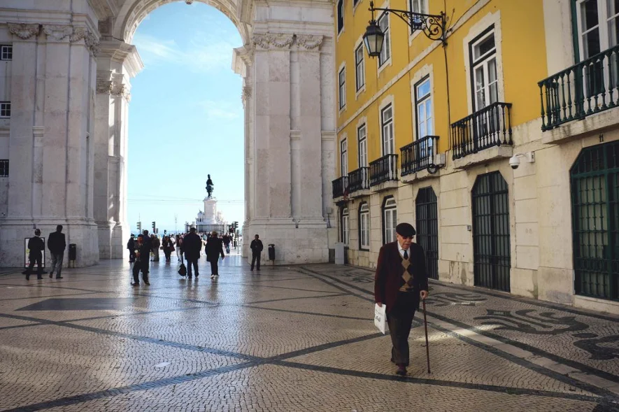 La entrada a la Plaza del Comercio en Lisboa con un señor mayor con boina andando con bastón.